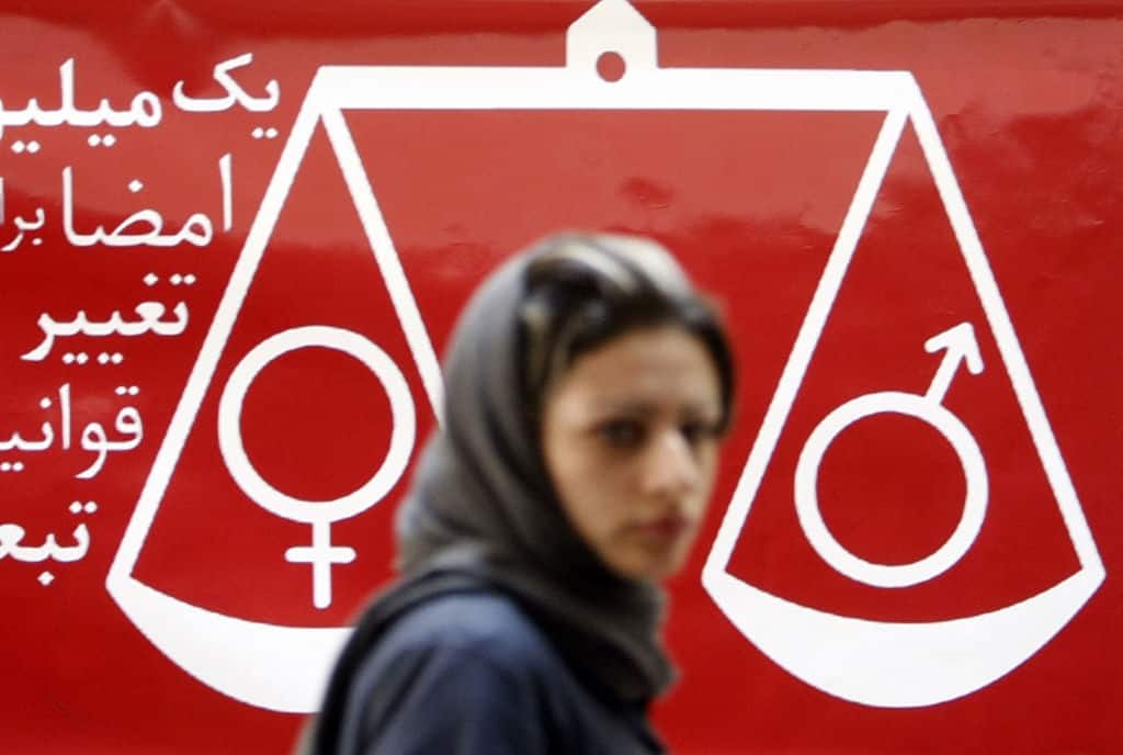 TOPSHOT - An Iranian woman walks past a banner reading "one million signatures to change the biased laws" and bearing a scale balancing female and male symbols during a press conference in Tehran, 27 August 2007. Iranians petitioning to achieve equal rights for women and men in Iran said today they hoped that their efforts would help change people's mentalities on the matter. AFP PHOTO/BEHROUZ MEHRI (Photo by Behrouz MEHRI / AFP) (Photo by BEHROUZ MEHRI-/AFP via Getty Images)          