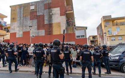 Spain's National Police officers stand as migrants wait on the sidewalk before being registered in Loma Colmenar district of Ceuta on August 31, 2026. Tensions remain high in the territory of 80,000 inhabitants since tens of thousands of people crossed into Ceuta from Morocco over several days in July, triggering a Europe-wide migrant alert. Spanish Prime Minister said the rush of migrants to the Spanish enclave was still under investigation, though he ruled out any responsibility on the part of Moroccan authorities. (Photo by Antonio Sempere / AFP) / The erroneous mention appearing in the metadata of this photo by Antonio Sempere has been modified in AFP systems in the following manner: [on August 31, 2026] instead of   [on August 27, 2026]. Please immediately remove the erroneous mention[s] from all your online services and delete it  from your servers. If you have been authorized by AFP to distribute it to third parties, please ensure that the same actions are carried out by them. Failure to promptly comply with these instructions will entail liability on your part for any continued or post notification usage. Therefore we thank you very much for all your attention and prompt action. We are sorry for the inconvenience this notification may cause and remain at your disposal for any further information you may require.