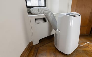 2WRXDBP a portable air conditioning unit on the floor of a shabby apartment with the vent duct attached to the window