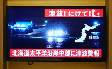 A tsunami warning is issued as a live footage of a boat leaving a coast port screens on a television in Sapporo, in Japan’s northern Hokkaido prefecture on December 8, 2025. Japan recorded a 40-centimetre (16-inch) tsunami after a 7.6-magnitude quake on December 8. (Photo by GREG BAKER / AFP)