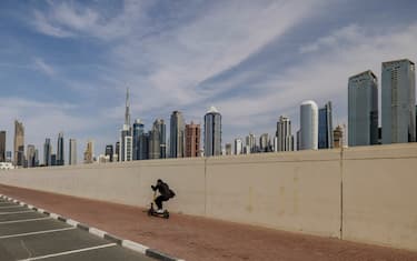 DUBAI, UNITED ARAB EMIRATES - March 11: 
A person rides an electric scooter along a sidewalk with Dubai's skyline, including the Burj Khalifa, rising in the background.
(Photo by Katarina Premfors / For The Washington Post via Getty Images)