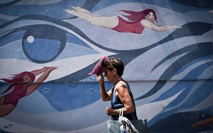 TOPSHOT - A pedestrian shelters from the sun with a handheld fan as she walks past a mural by the artists Maria Ginzburg and Gaetano Matrella, downtown Rome, on July 19, 2023, amid a heat wave in Italy. (Photo by Tiziana FABI / AFP) / RESTRICTED TO EDITORIAL USE - MANDATORY MENTION OF THE ARTIST UPON PUBLICATION - TO ILLUSTRATE THE EVENT AS SPECIFIED IN THE CAPTION (Photo by TIZIANA FABI/AFP via Getty Images)