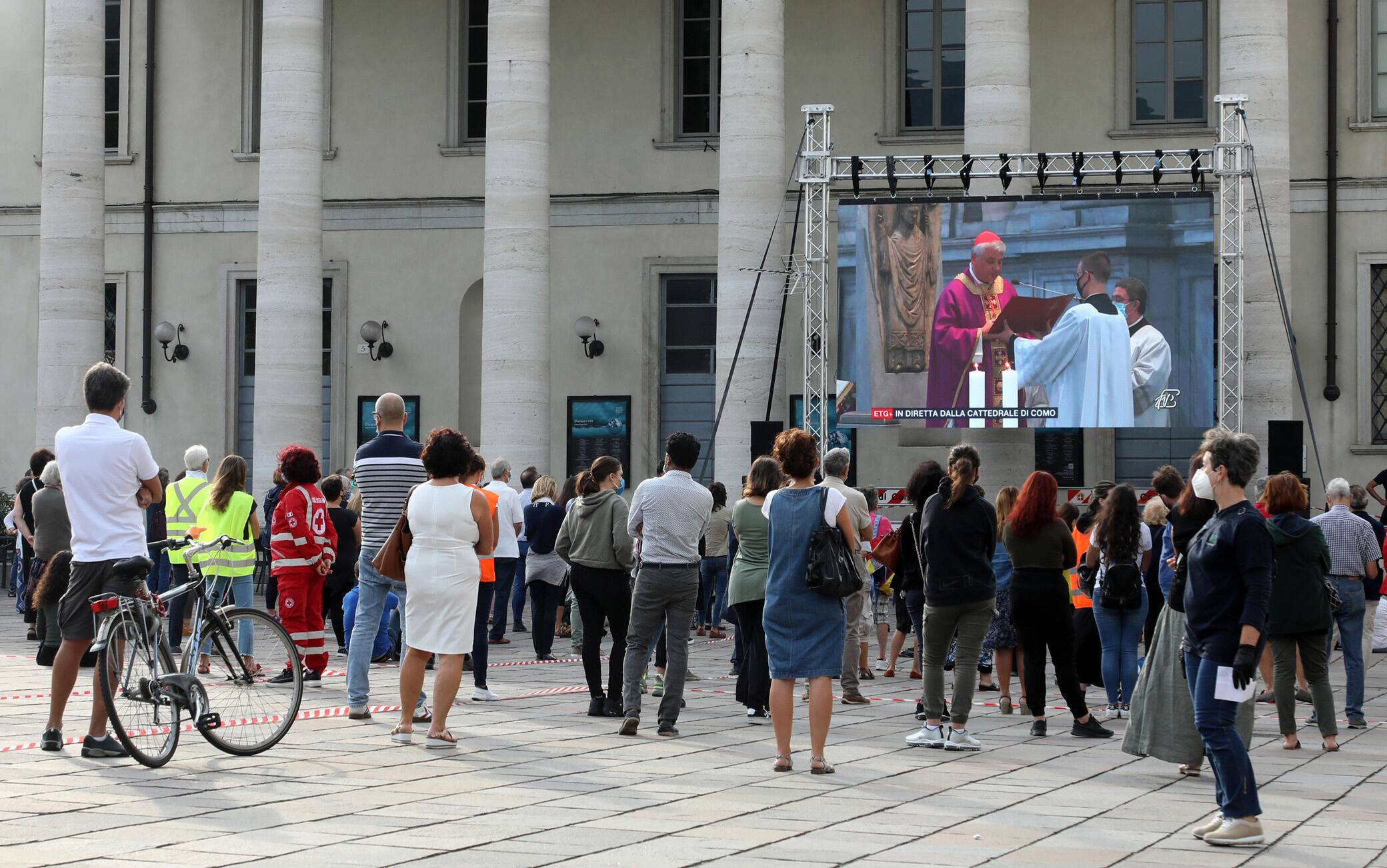 Alcune persone seguono su uno dei maxi schermi che sono stati allestiti nel centro di Como in occasione dell'orazione funebre per don Roberto Malgesini il parrocco assassinato da una delle persone di cui si prendeva cura. Como 19 Settembre 2020.ANSA / MATTEO BAZZI