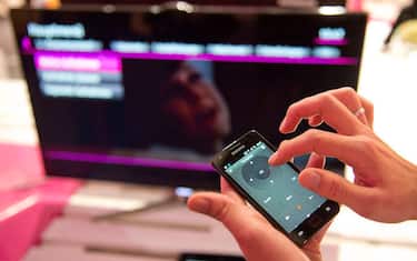 An emplyee flicks through tv channels with his smartphone at the Deutsche Telekom booth during the 52nd edition of the "IFA" (Internationale Funkausstellung) trade fair in Berlin on August 30, 2012. IFA, Europe's largest consumer electronics and home appliances fair opens to the public from August 31 to September 5, 2012, with more than 1,400 exhibitors unveiling the latest touch-screen tablets, 3D televisions without special glasses and smaller, smarter and more interconnected devices to wow punters.     AFP PHOTO / ODD ANDERSEN        (Photo credit should read ODD ANDERSEN/AFP/GettyImages)