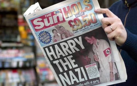 A man reads, 13 January 2005 in Paris, the British tabloid The Sun featuring Harry, 20, the younger son of Prince Charles and the late Princess Diana, wearing a khaki uniform with an armband emblazoned with a swastika, emblem of the German WWII Nazi Party. The photographs in The Sun newspaper triggered outrage, especially from the Jewish community which pointed out that they appear as the royal family prepares to lead commemorations of the 60th anniversary of the Holocaust. AFP PHOTO GABRIEL BOUYS (Photo by GABRIEL BOUYS / AFP) (Photo by GABRIEL BOUYS/AFP via Getty Images)