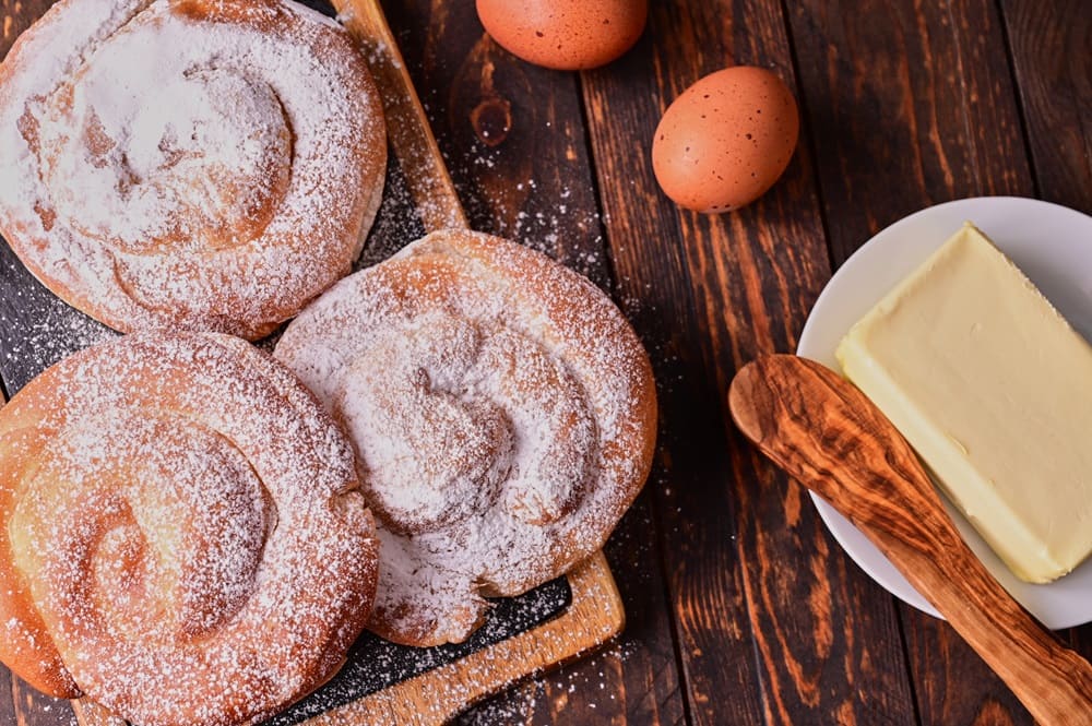 Ensaimadas, typical pastry of Mallorca, and its main ingredientrs: butter and eggs on wooden board