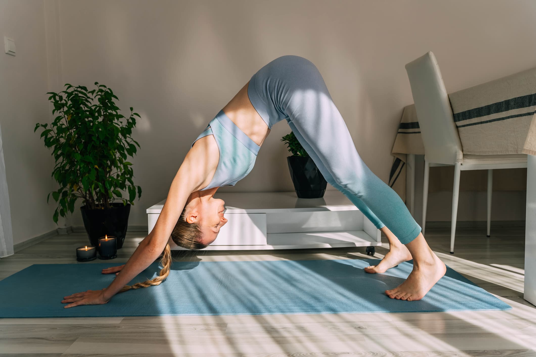 Mid adult woman doing yoga at home on a sunny day. Indoor plants in the background.