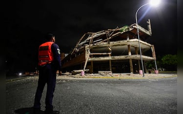 A Venezuelan municipal police officer stands next to a collapsed building following an earthquake in Valencia, Venezuela on June 24, 2026. Two earthquakes of magnitude 7.2 and 7.5 struck the same area of Venezuela on the evening of June 24, causing buildings to collapse, according to the United States Geological Survey (USGS) and AFP journalists. The quakes drove residents of the capital, Caracas, into the streets. (Photo by Jacinto OLIVEROS / AFP)