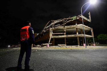 A Venezuelan municipal police officer stands next to a collapsed building following an earthquake in Valencia, Venezuela on June 24, 2026. Two earthquakes of magnitude 7.2 and 7.5 struck the same area of Venezuela on the evening of June 24, causing buildings to collapse, according to the United States Geological Survey (USGS) and AFP journalists. The quakes drove residents of the capital, Caracas, into the streets. (Photo by Jacinto OLIVEROS / AFP)