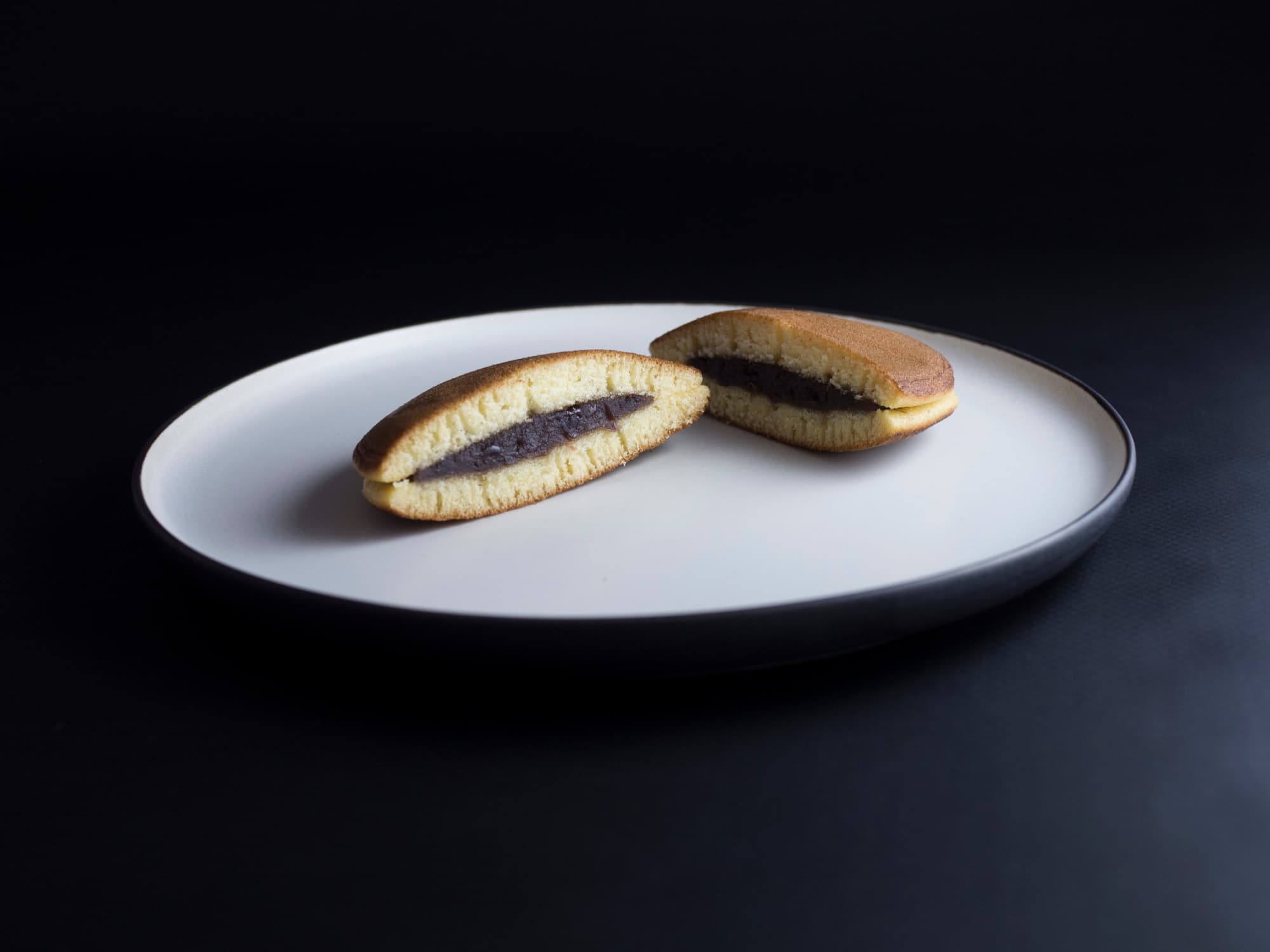 Dorayaki - Japanese cake made from two small "pancakes", filled with a red bean paste. Cut in halves and served on rustic plate. Isolated on black background.